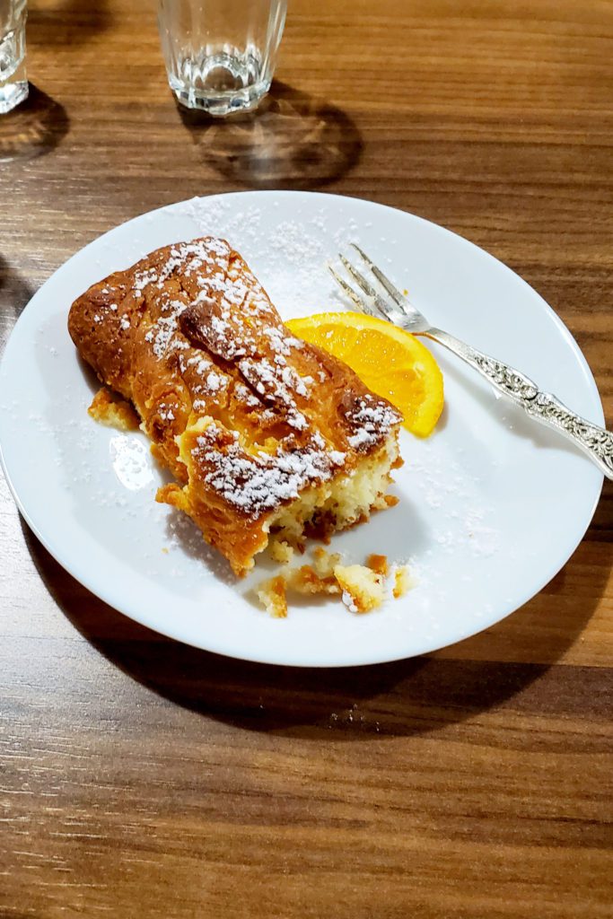 This is an image of the portokalopita garnished with an orange slice and powdered sugar. Traveling and food in Greece. 