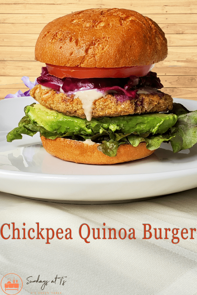 This is an image of the chickpea quinoa burger. It is layered with lettuce, avocado, the burger, a tahini dressing, red pickled cabbage, and tomato.
