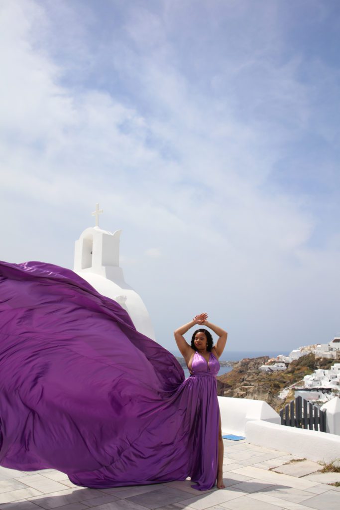 This is an image of T in a purple flying dress while traveling in Greece, specifically in Oia on Santorini. 