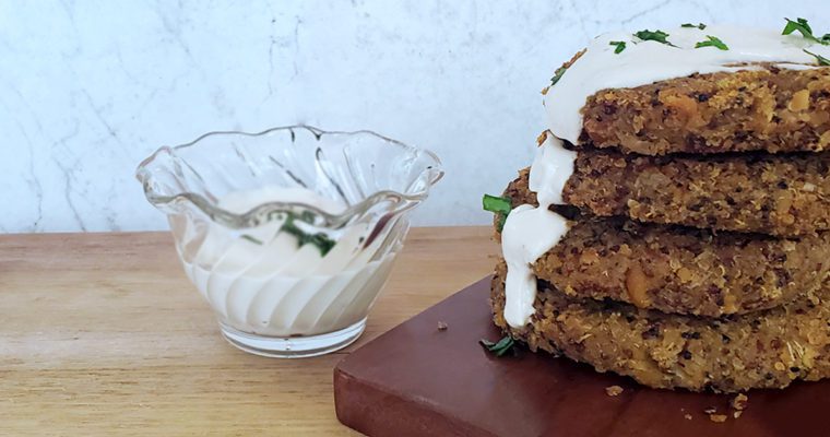 This is an image of 4 chickpea quinoa burgers stacked and topped with a lemon garlic tahini dressing.