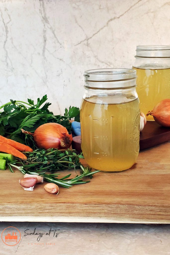 This is an image of two containers of vegetable broth staged with ingredients, including onions, garlic, carrots, celery, and herbs.
