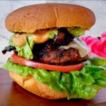 This is an image of the finished chorizo burger, topped with Sweet Sriracha Glazed Bacon, Homemade Guacamole, Chipotle Mayo, pepper jack cheese, tomato, and lettuce.