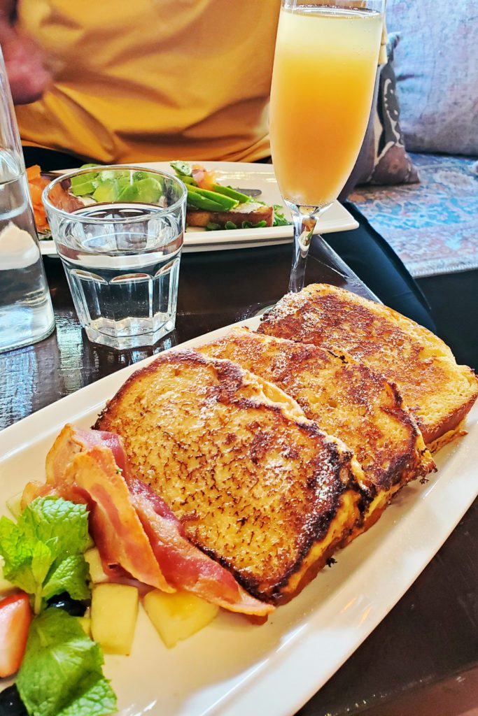 This is an image of the gluten-free French Toast with the gluten-free avocado toast in background and a mimosa at Senza Gluten by Jemiko Café and Bakery in New York City.