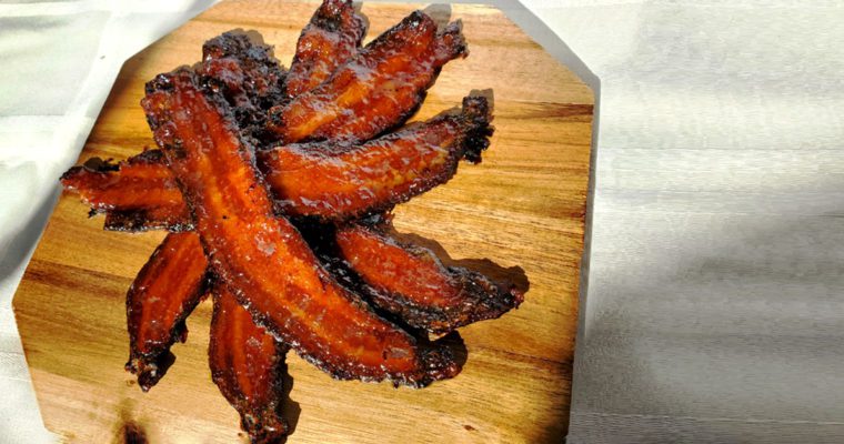This is an image of the sweet sriracha glazed bacon with crispy ends and served on a wooden platter.