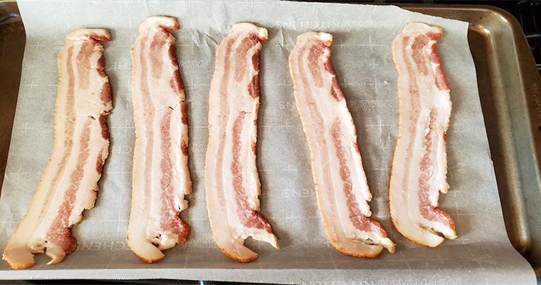 This is an image of thick cut bacon on a baking sheet lined with parchment paper before par-cooking.