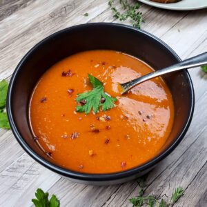 This is an image of a bowl of roasted red pepper chickpea soup garnished with red pepper flakes and fresh parsley.