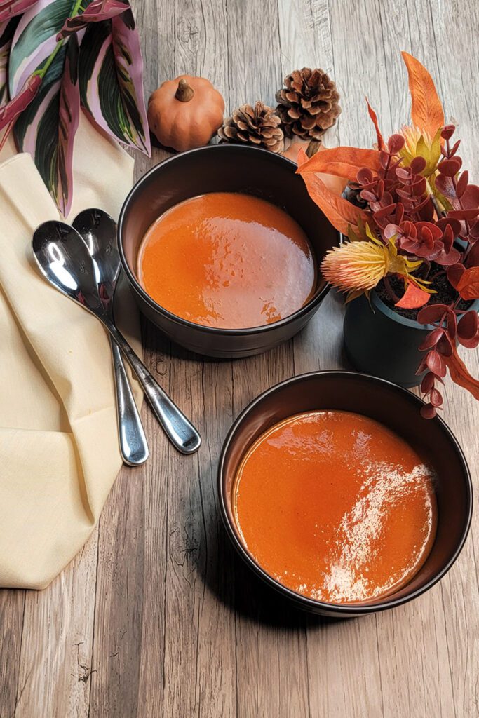 This is an image of two bowls of roasted red pepper chickpea soup decorated with fall foliage.