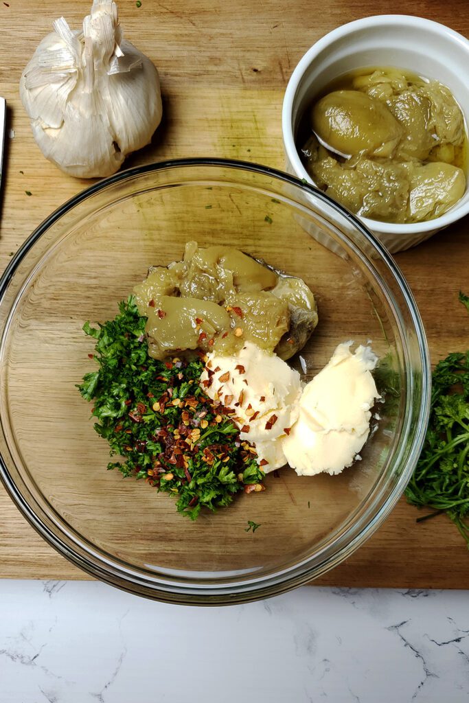 This is an image of the ingredients for the garlic confit toast, including the garlic confit, fresh parsley, vegan butter, and red chili flakes. 