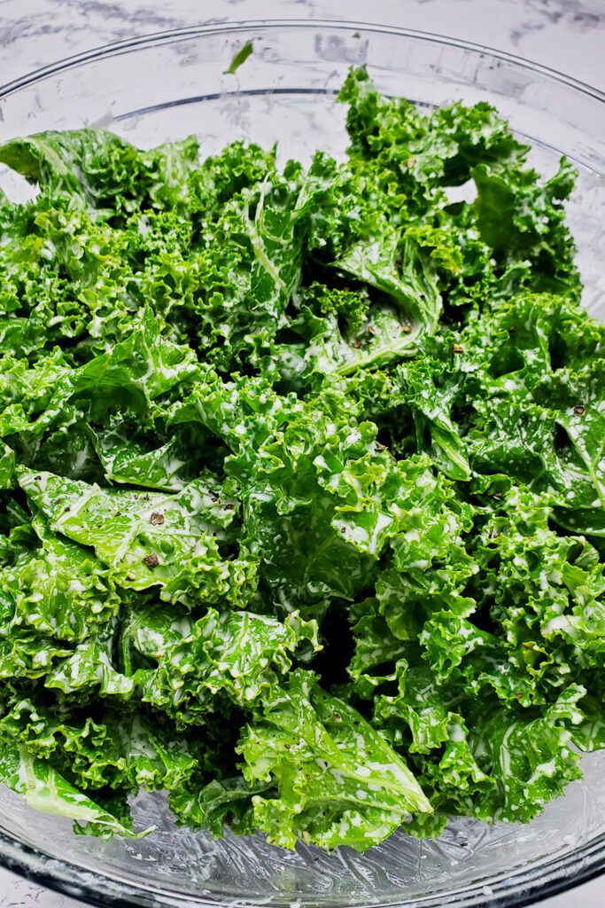 This is an image of the kale salad with tahini dressing and fresh cracked pepper in a clear bowl.