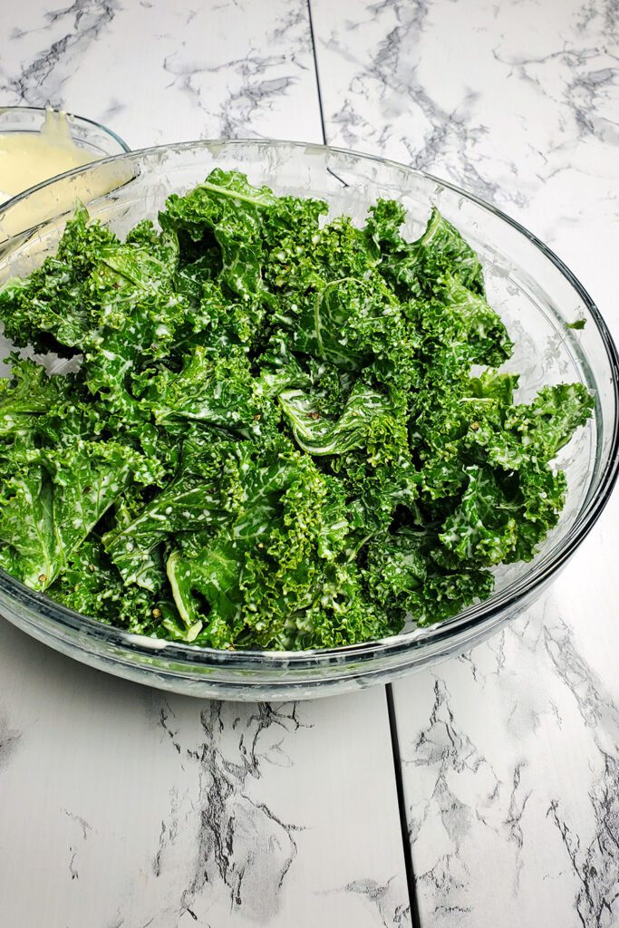This is an image of the kale salad with tahini dressing and fresh cracked pepper in a clear bowl. The tahini dressing is in the background.