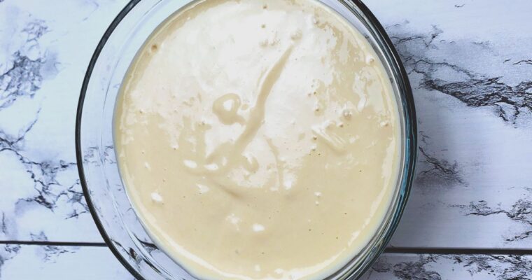 This is an image showing the creamy texture of the tahini dressing in a clear bowl with a spoon.