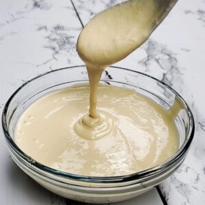 This is an image showing the creamy texture of the tahini dressing in a clear bowl with a spoon.