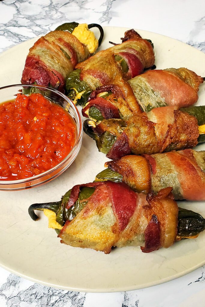 This is an image of stuffed bacon jalapenos from Sundays at T's. These jalapeno poppers are stuffed with three cheeses (cream cheese, pepper jack cheese, and cheddar cheese), paprika, and garlic.