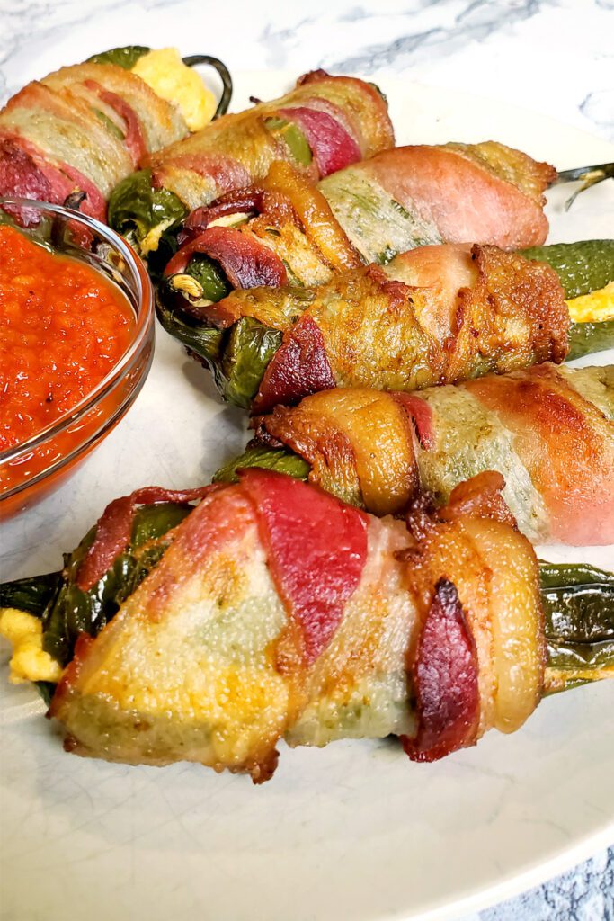 This is an image of stuffed bacon jalapenos from Sundays at T's. These jalapeno poppers are stuffed with three cheeses (cream cheese, pepper jack cheese, and cheddar cheese), paprika, and garlic.