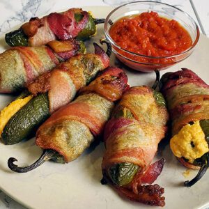 This is an image of stuffed bacon jalapenos from Sundays at T's. These jalapeno poppers are stuffed with three cheeses (cream cheese, pepper jack cheese, and cheddar cheese), paprika, and garlic.