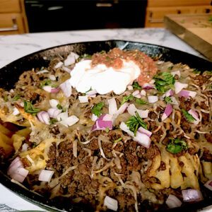 This is an image of Sundays at T's waffle fry nachos topped with seasoned ground beef, a 4 cheese Mexican blend, onions, sour cream, salsa, and fresh cilantro.