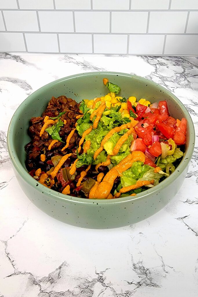 This is an image of the vegan taco bowl with the lentil taco "meat", black beans, lettuce, corn, guacamole, salsa, and chipotle aioli.