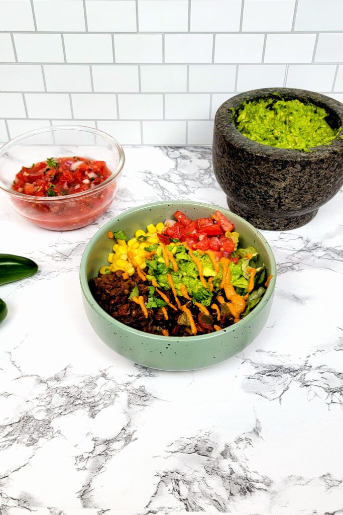 This is an image of the vegan taco bowl with the lentil taco "meat", black beans, lettuce, corn, guacamole, salsa, and chipotle aioli.