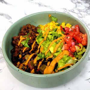 This is an image of the vegan taco bowl with the lentil taco "meat", black beans, lettuce, corn, guacamole, salsa, and chipotle aioli.