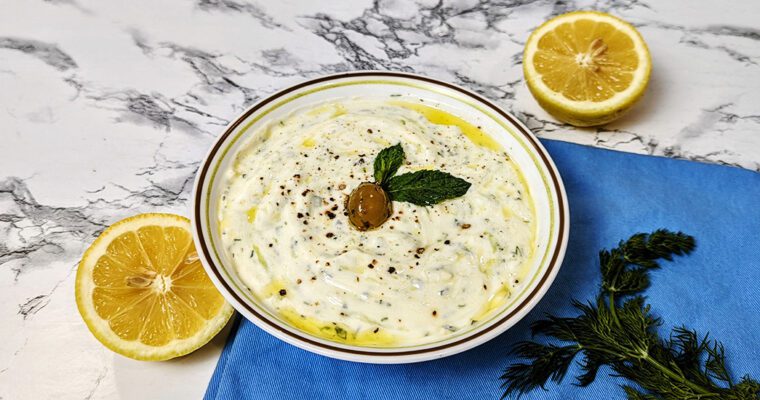 This is an image of the Greek Tzatziki by Sundays at T's. The tzatziki is garnished with fresh mint, a Kalamata olive, and fresh cracked pepper.