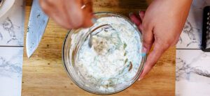 This is an image of T of Sundays at T's mixing in the cucumber, fresh herbs, and minced garlic into the Greek yogurt for a delicious Greek tzatziki.