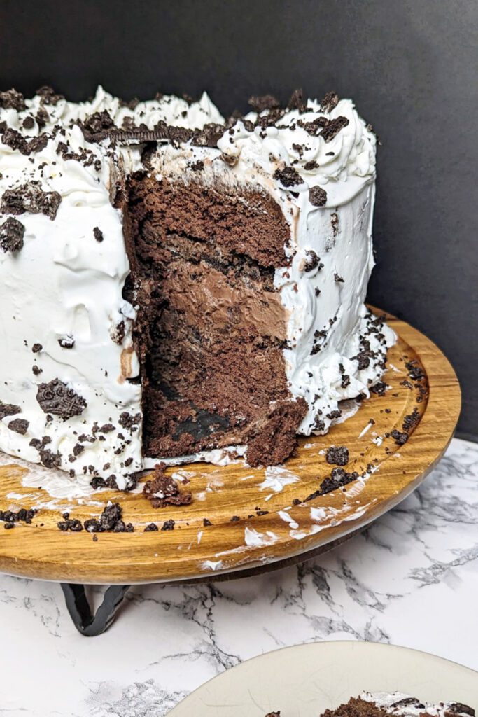 This is an image of the gluten-free 5-layer chocolate ice cream cake. This death by chocolate ice cream cake is made with a gluten-free chocolate cake, gluten-free Oreos, chocolate ice cream, chocolate syrup, Reese's peanut butter ice cream topping, and whipped cream. This image shows a the whole cake with a slice "missing" to show the inside of the cake.
