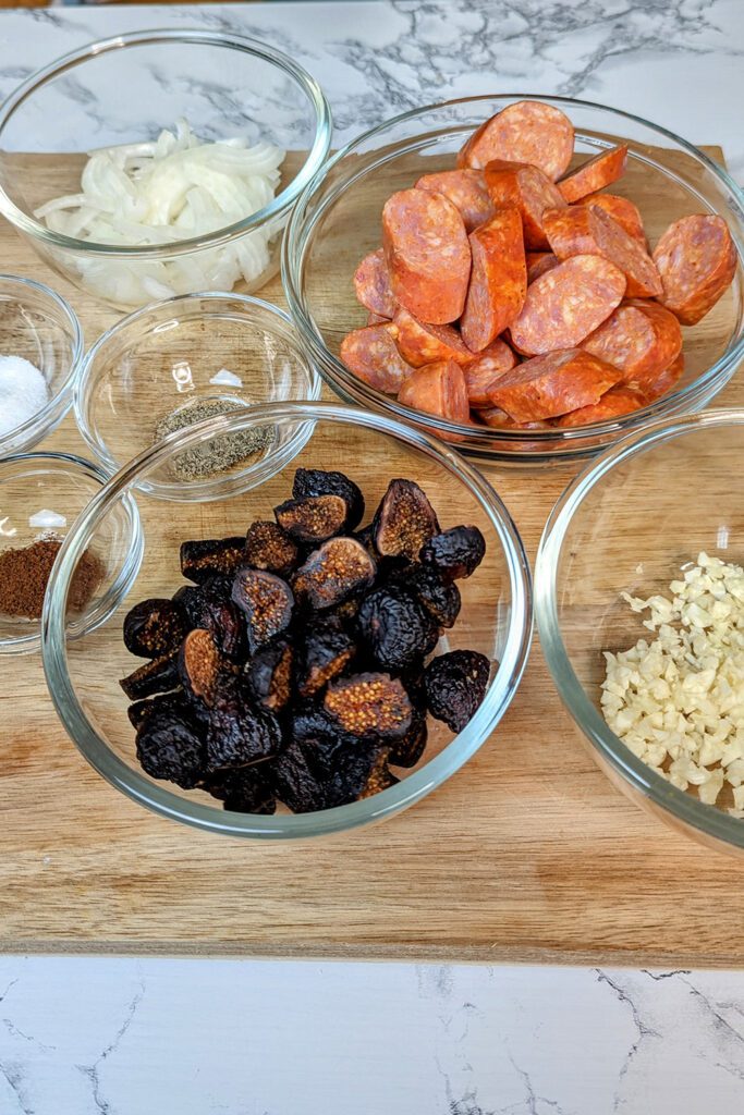 This is an image of the ingredients to make chorizo and fig tapas. Onions, chorizo, figs, garlic, salt, pepper, ground cloves, cinnamon stick, red wine, and beef stock.