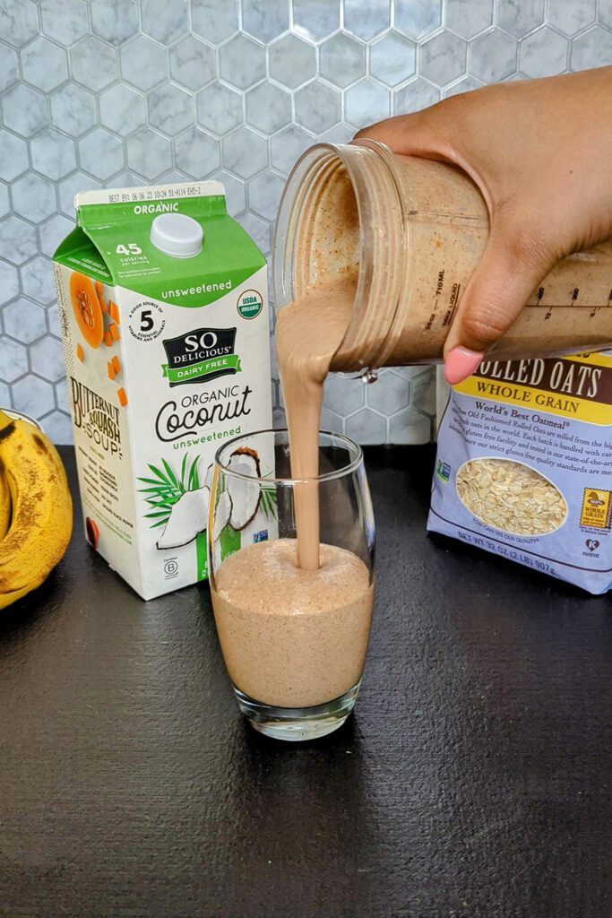 This is an image of the chocolate chia banana smoothie from Sundays at T's. The smoothie is being poured into a class and the image is staged with So Delicious Organic Coconut milk, Bob's Red Mill gluten-free rolled oats, and bananas.